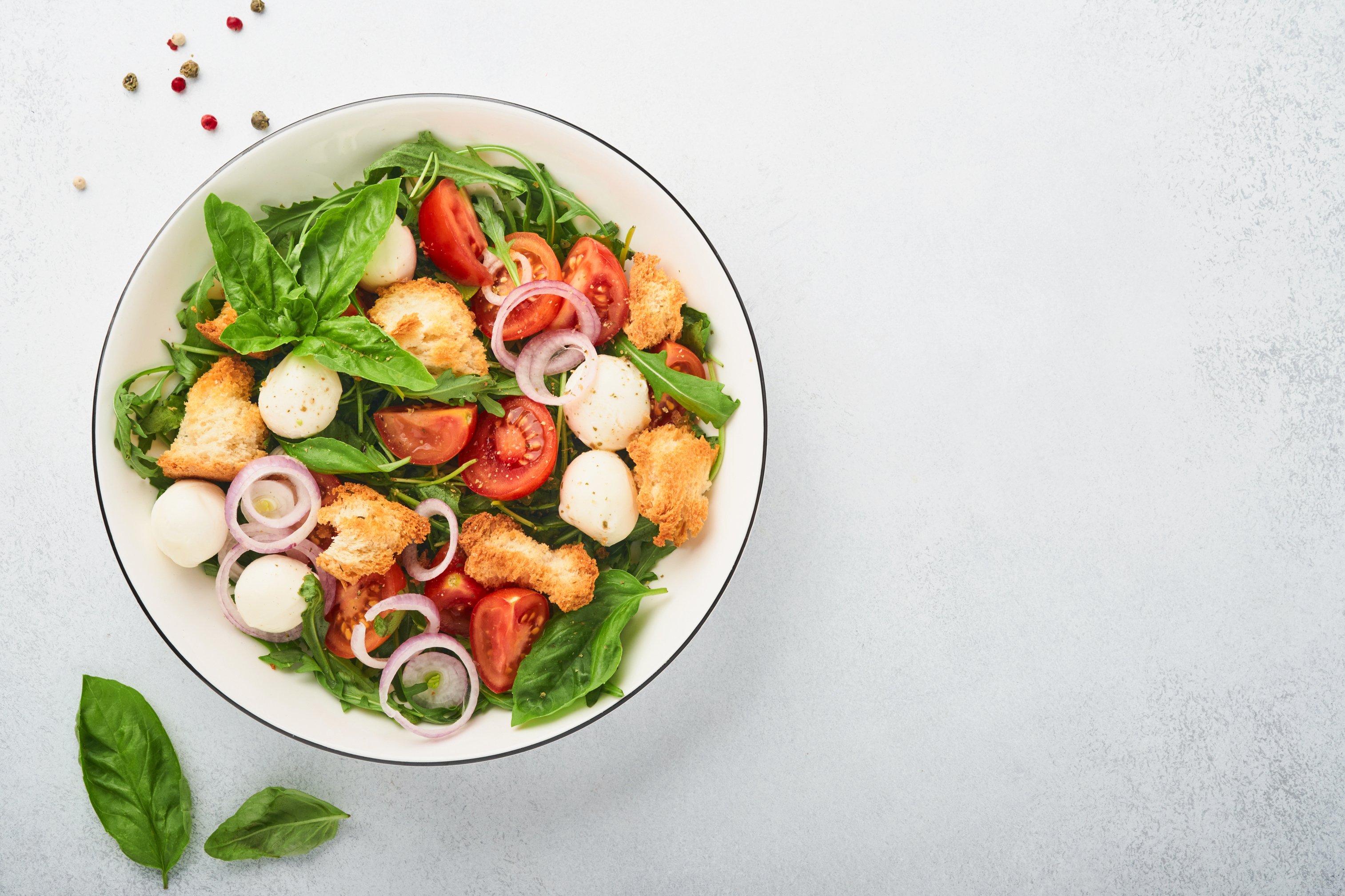 Panzanella Bread Salad. Traditional Food of Italy with Tomatoes, Mozzarella Balls, Basil, Onion and Bread on Light Grey Background. Traditional Italian Cooking. Top View. Copy Space.